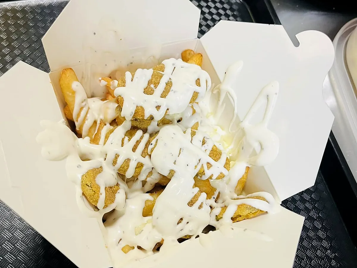 Poutine topped with crispy fried pickle chips and a ranch drizzle in an open takeout box