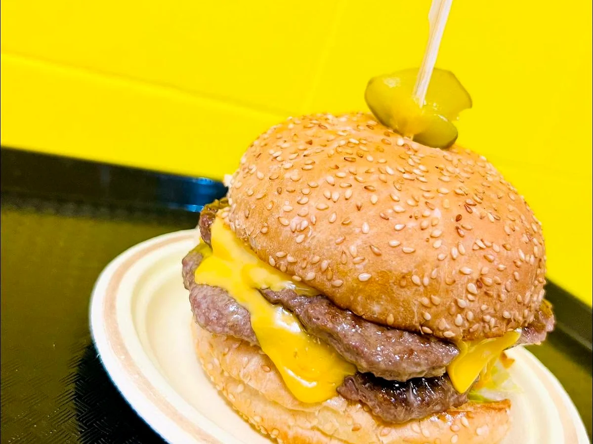 Double smash burger with two thin seared beef patties and melted American cheese on a sesame bun, topped with a pickle skewer