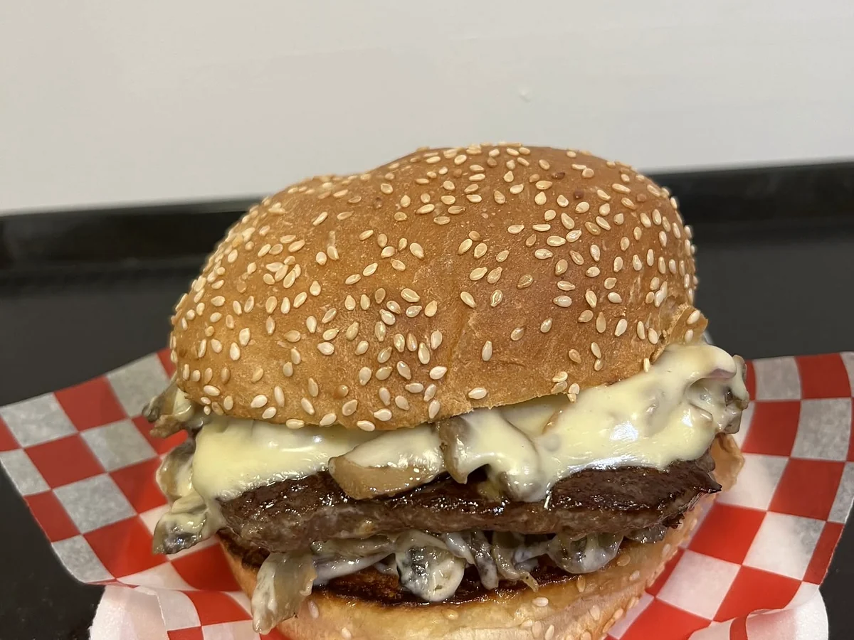 Smash burger with melted Swiss cheese and sauteed mushrooms on a sesame bun, on red and white checkered paper