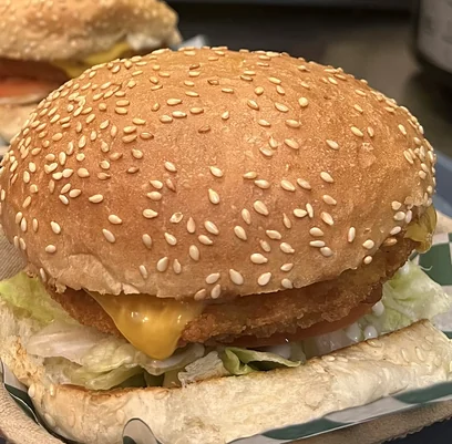 Crispy breaded chicken burger with cheese, lettuce and tomato on a sesame bun