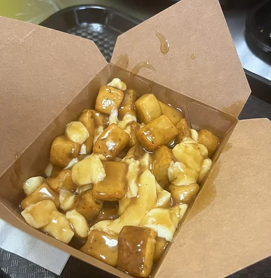 Poutine with thick gravy and cheese curds in an open kraft takeout box